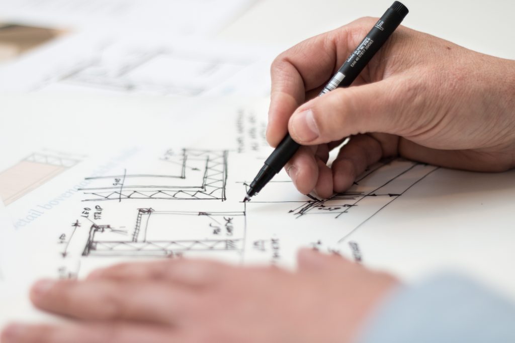 An image showing two hands sketching architect drawings on a large sheet of white paper