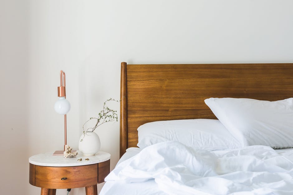 An image showing a white bedroom with wooden bed and side table in a loft conversion