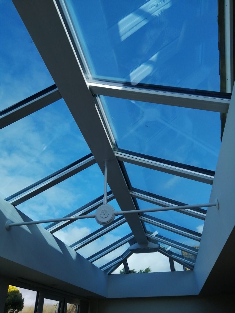 Conservatory roof blind rolled back on a peaked glass roof window