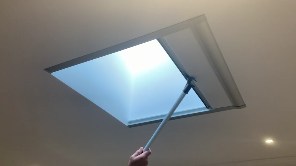 A hand and blind opening pole closing a skylight blind